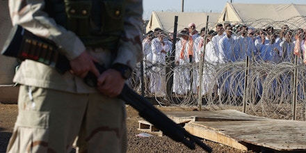 ABU GHRAIB, IRAQ - SEPTEMBER 26:  A U.S. soldier stands guard as Iraqi detainees stand in line waiting to be processed for release from Abu Ghraib prison facility on September 26, 2005 in Abu Ghraib, 21 miles west of Baghdad, Iraq. The U.S. military released about 500 detainees from Abu Ghraib prison on September 26 at the request of the Iraqi government prior to the start of the holy Muslim month of Ramadan. (Photo by Wathiq Khuzaie/Getty Images)