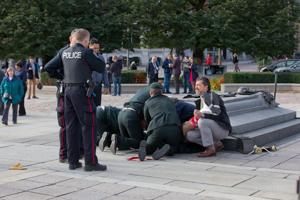 Image #: 32693473    OTTAWA, CANADA - OCTOBER 22: Police, bystanders and soldiers aid a fallen soldier at the War Memorial as police respond to an apparent terrorist attack  on October 22, 2014 in Ottawa, Canada.  A GUNMAN is believed to have shot a soldier as he was standing guard at the National War Memorial in Ottawa, Canada, this morning (Wednesday, October 22). It is believed police then chased the man into the main parliament building at Parliament Hill, where more shots were fired. Police are hunting the streets and buildings for further suspects and have asked the public to stay away from the area. There is also a report of shootings at the Rideau Centre mall in downtown, a short distance from the War Memorial. The wounded soldier was taken into an ambulance and treated by medical personnel and is condition is unclear. The incident comes after Canada raised its terror threat level from low to medium after a Muslim convert deliberately ran over two soldiers, killing one of them.     Wayne Cuddington/Barcroft Media /Landov
