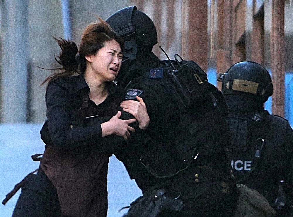 FILE - In this Dec. 15, 2014 file photo, a hostage runs to an armed tactical response police officers for safety after she escaped from a cafe under siege at Martin Place in the central business district of Sydney, Australia.  The man who took 18 people hostage at a Sydney cafe last year was educated and erratic, secretive about his own life and public about his many grievances, and a self-obsessed fabulist who grew increasingly defiant as he edged closer to launching his deadly attack, lawyers told an inquest Monday, May 25, 2015. (AP Photo/Rob Griffith, File)