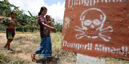 A Cambodian woman (C) carrying a baby walks by landmine awareness sign at O'Chhoeu Kram village in the former Khmer Rouge's stronghold Pailin near the Thai border some 375 kilometers north west of the capital Phnom Penh, 21 July 2007.  Nearly 30 years after the Khmer Rouge were pushed from power and following a decade of contentious negotiations, Cambodia appears poised to finally seek justice for the crimes committed during the regime's 1975-79 rule after prosecutors file cases against five former Khmer Rouge leaders .   AFP PHOTO / TANG CHHIN SOTHY (Photo credit should read TANG CHHIN SOTHY/AFP/Getty Images)