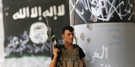 A member of Iraqi counterterrorism forces stands guard near Islamic State militant graffiti in Fallujah, Iraq, Monday, June 27, 2016. Thick clouds of black smoke billowed over northwest Fallujah Monday as dozens of homes continued to burn a day after the city was declared “fully liberated” from the Islamic State group. Iraqi special forces Lt. Gen. Abdel Wahab al-Saadi who led the operation to retake the city, said that IS militants torched hundreds of houses in Fallujah's north and west as they fled Sunday, just as the fighters did in many of the city's other neighborhoods over the course of the operation. (AP Photo/Hadi Mizban)