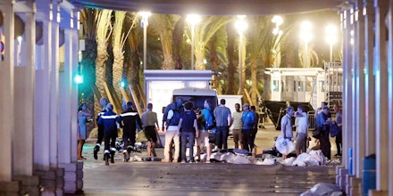 People stand next to covered bodies in the early hours of Friday, July 15, 2016, on the Promenade des Anglais in Nice, southern France.  France has been stunned again as a large white truck killed many people after it mowed through a crowd of revelers gathered for a Bastille Day fireworks display late Thursday evening, in the Riviera city of Nice. (AP Photo)