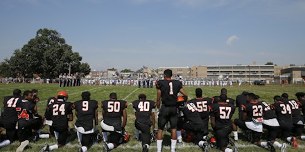 Woodrow Wilson High's Edwin Lopez (#1) stands while some of his teammates kneel during the national anthem before Woodrow Wilson High School played Highland High School at Woodrow Wilson High School in Camden, N.J., Saturday, Sept. 10, 2016. Colin Kaepernick's protest against social injustices has opened discussion and debate on a national level. For high schools across the country, where a host of football players have joined the San Francisco quarterback by kneeling during the national anthem, the issue is much more personal and complicated.  (Yong Kim/The Philadelphia Inquirer via AP)