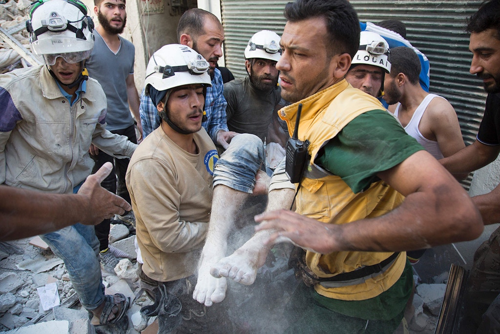 Syrian civil defense volunteers, known as the White Helmets, carry a body after digging it out from under the rubble of a building following a reported airstrike in the northern city of Aleppo on July 23, 2016.