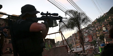 RIO DE JANEIRO, BRAZIL - MAY 13:  An officer from the CORE police special forces aims his weapon during an operation to search for fugitives in the Complexo do Alemao pacified community, or 'favela' on May 13, 2014 in Rio de Janeiro, Brazil. Ahead of the 2014 FIFA World Cup, Rio has seen an uptick in violence in its pacified slums. A total of around 1.6 million Rio residents live in shantytowns, many of which are controlled by drug traffickers.  (Photo by Mario Tama/Getty Images)