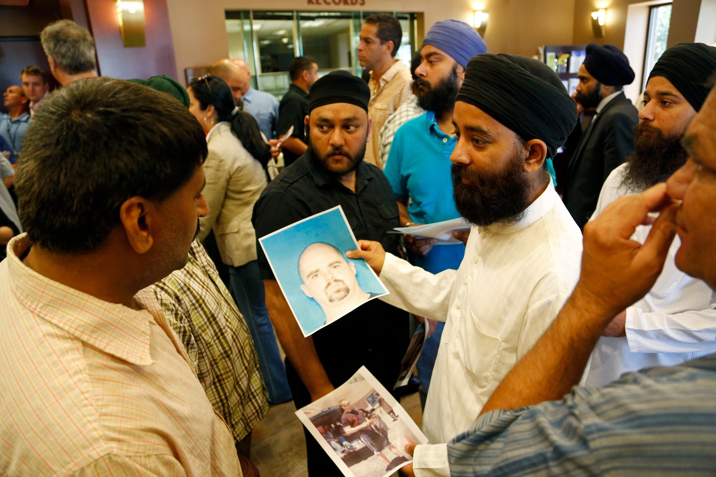 OAK CREEK, WI - AUGUST 6: Members of the community hold up the mug shot handed out by the FBI of the suspected shooter Wade Michael Page after a press conference on the shooting at the Sikh Temple of Wisconsin where yesterday a gunman fired upon people at service August, 6, 2012 in Oak Creek, Wisconsin. At least six people were killed when the shooter identified as Wade Michael Page opened fire on congregants in the Milwaukee suburb. The suspect who was a United States Army veteran was killed in a shootout with  police.  (Photo by Darren Hauck/Getty Images)