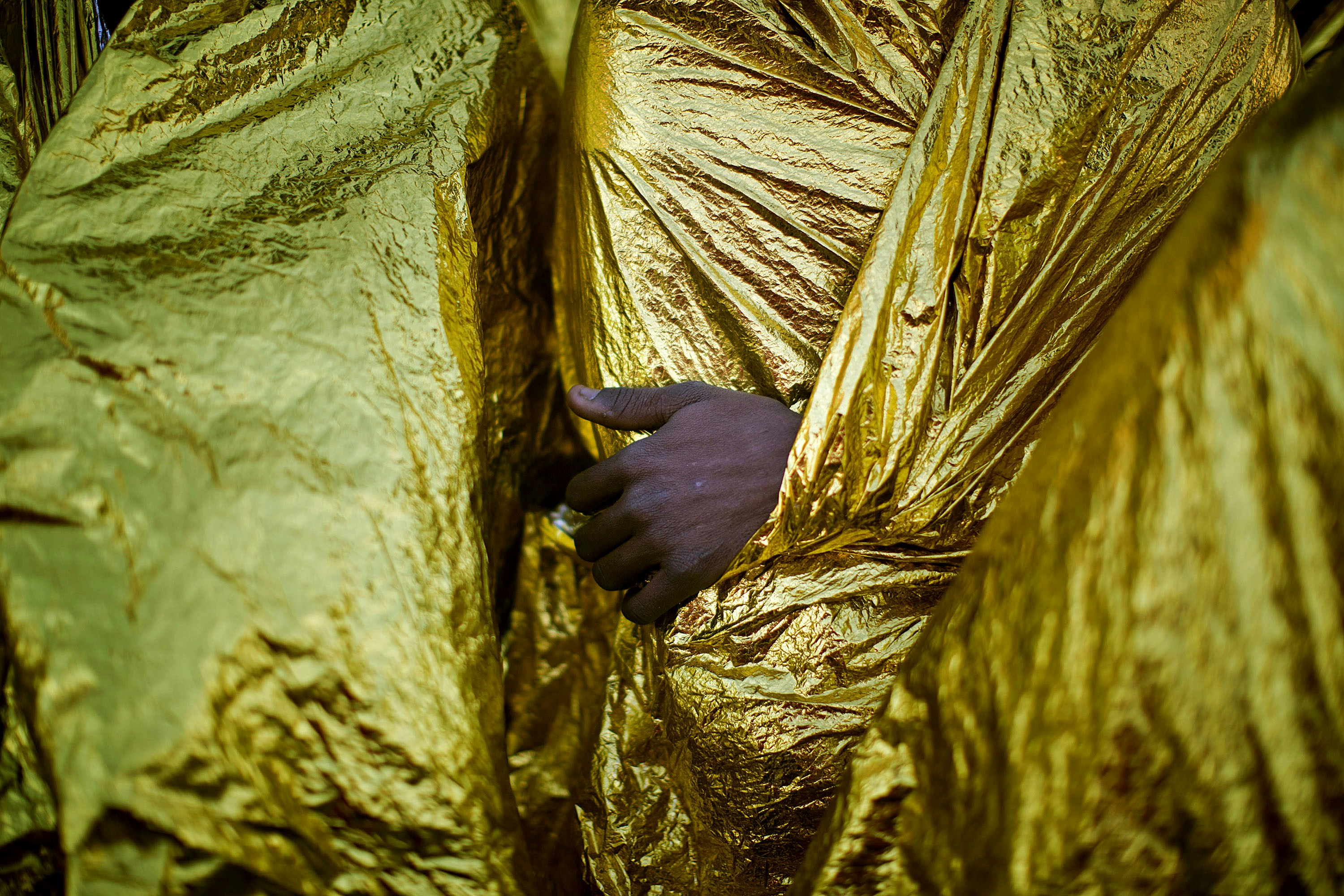 The hand of an Sub-Saharan migrant is seen outside the blanket as men sit on the deck of the Golfo Azzurro rescue vessel after arriving at the port of Messina, in Italy, with more than 299 migrants aboard the ship rescued by members of Proactive Open Arms NGO, on Sunday, Jan. 29, 2017. (AP Photo/Emilio Morenatti)