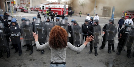 BALTIMORE, MD - APRIL 27:  A woman faces down a line of Baltimore Police officers in riot gear during violent protests following the funeral of Freddie Gray April 27, 2015 in Baltimore, Maryland. Gray, 25, who was arrested for possessing a switch blade knife April 12 outside the Gilmor Homes housing project on Baltimore's west side. According to his attorney, Gray died a week later in the hospital from a severe spinal cord injury he received while in police custody.  (Photo by Chip Somodevilla/Getty Images)