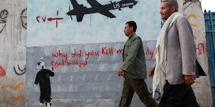 Yemeni men walk past a mural depicting a US drone and reading 