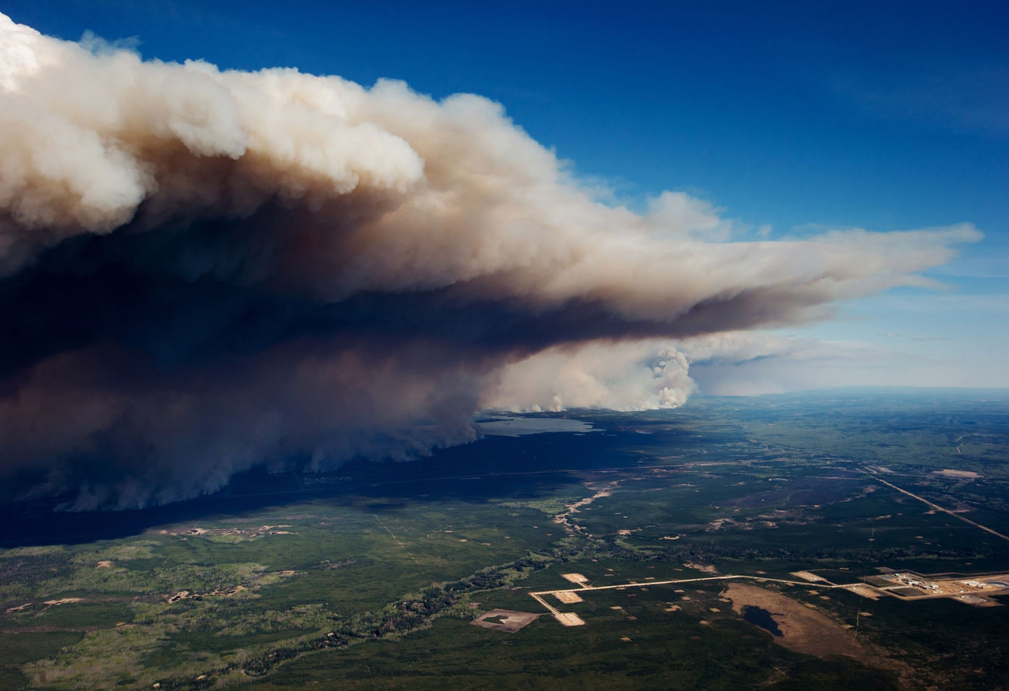 A huge plume of smoke from wildfires burning rises over Fort McMurray in this aerial photograph taken in Alberta, Canada, on Friday, May 6, 2016. The wildfires ravaging Canada's oil hub in northern Alberta have rapidly spread to an area bigger than New York city, prompting the air lift of more than 8,000 evacuees as firefighters seek to salvage critical infrastructure. Photographer: Darryl Dyck/Bloomberg via Getty Images