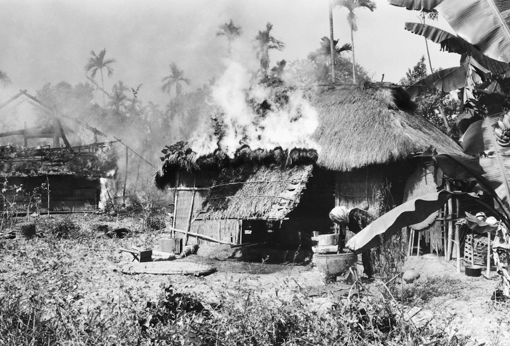 An old Vietnamese woman reaches into large jar to draw water in an attempt to fight flames consuming her home in a village 20 miles southwest of Da Nang, South Vietnam on Feb. 14, 1967. (AP Photo)