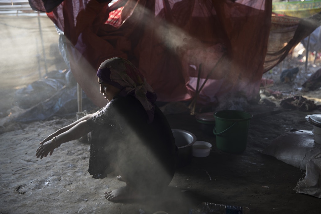 THAINKHALI, BANGLADESH - SEPTEMBER 25:  Sajida Begum, 18, sits in her makeshift tent, washing rice for dinner as smoke catches the late afternoon light September 25, 2017 in Thainkhali camp, Cox's Bazar, Bangladesh. Over 429,000 Rohingya refugees have fled into Bangladesh since late August during the outbreak of violence in Rakhine state as Myanmar's de facto leader Aung San Suu Kyi downplayed the crisis during a speech in Myanmar this week faces and defended the security forces while criticism on her handling of the Rohingya crisis grows. Bangladesh's prime minister, Sheikh Hasina, spoke at the United Nations General Assembly last week, focusing on the humanitarian challenges of hosting the minority Muslim group who currently lack food, medical services, and toilets, while new satellite images from Myanmar's Rakhine state continue to show smoke rising from Rohingya villages.  (Photo by Paula Bronstein/Getty Images)