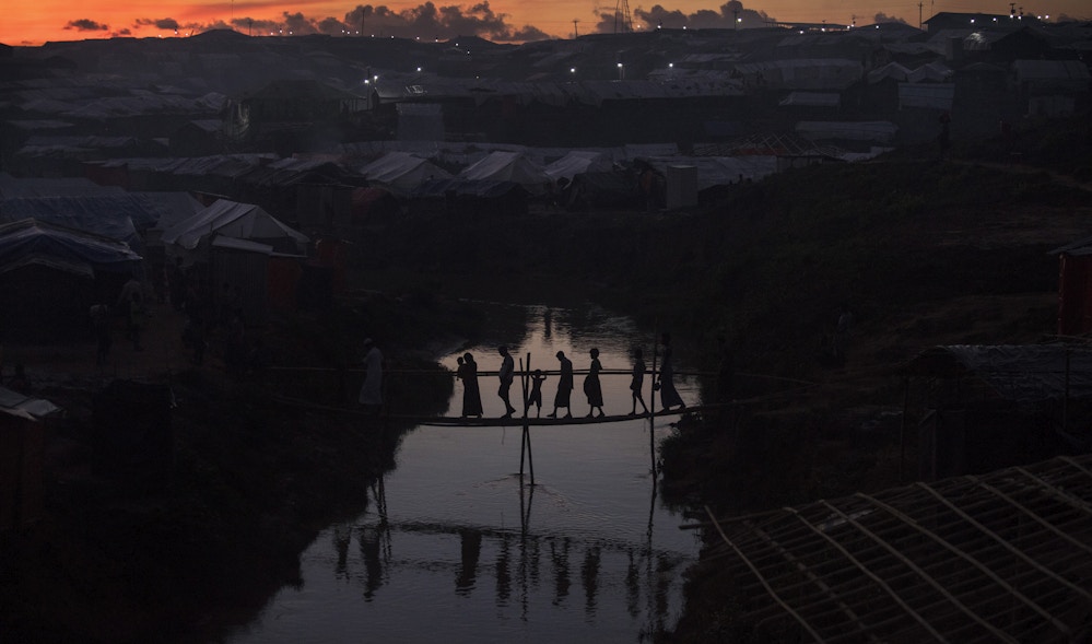 KUTUPALONG, BANGLADESH - OCTOBER 13: People cross a bamboo bridge over a stream as the sun sets on October 13, 2017 at the Kutuplaong refugee camp, Cox's Bazar, Bangladesh. According to UN sources around 519,000 Rohingya refugees had fled across the border from Myanmar to Bangladesh since 25 August. Thousands more remain stranded in Myanmar without the means to cross the border into Bangladesh. (Photo by Paula Bronstein/Getty Images)