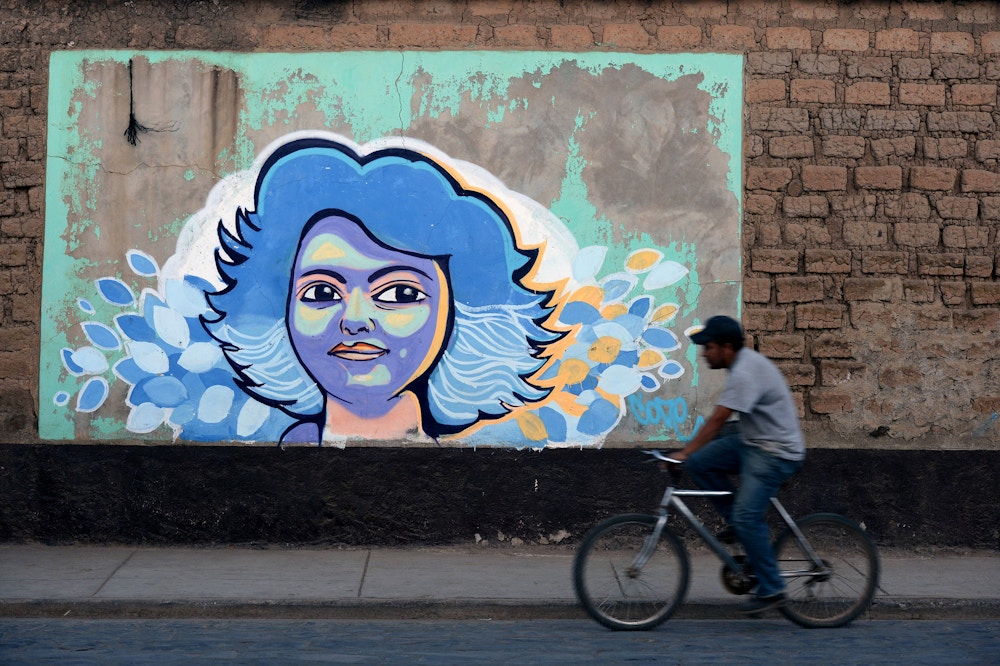 TOPSHOT - A man rides a bike past graffiti of Honduran indigenous environmentalist Berta Caceres a year after her murder, in La Esperanza, 180 km west of Tegucigalpa, on March 2, 2017. Caceres, an organizer of the Lenca people, the largest native group in Honduras, was murdered on March 3, 2016 in this city. / AFP PHOTO / ORLANDO SIERRA (Photo credit should read ORLANDO SIERRA/AFP/Getty Images)