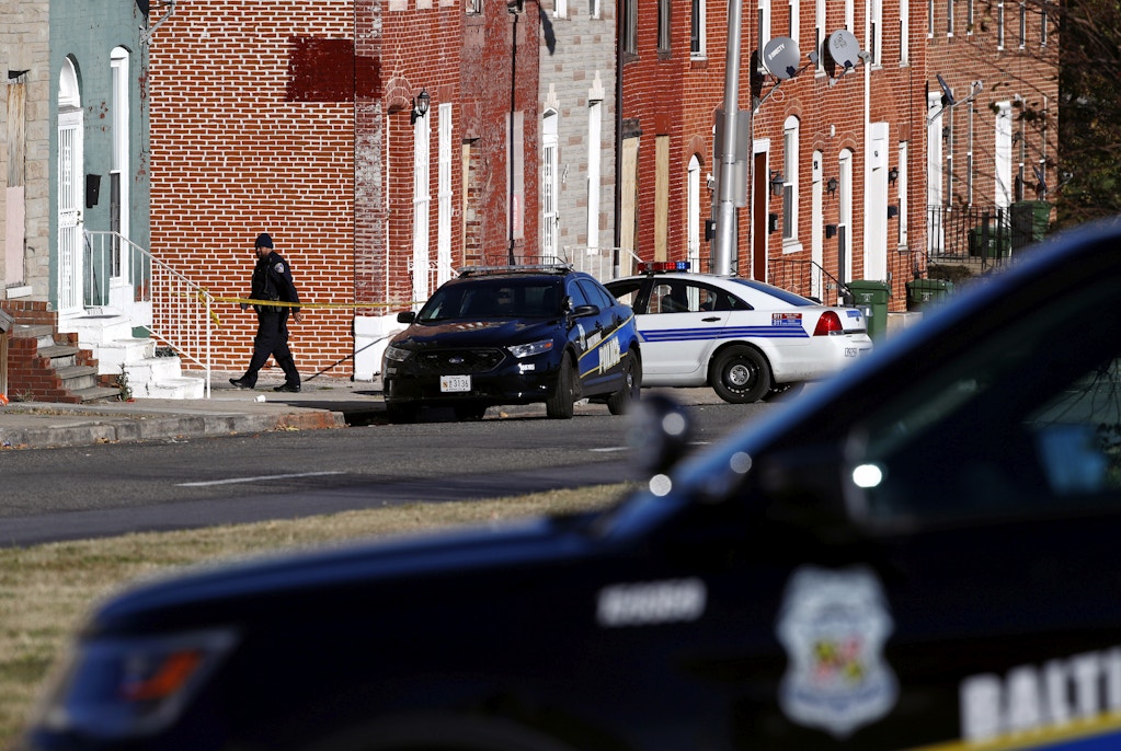 A member of the Baltimore Police Department walks behind a police line near the scene of the shooting death of Baltimore Police detective Sean Suiter in Baltimore, Friday, Nov. 17, 2017. The manhunt for Suiter's killer has entered its third day. Suiter was shot Wednesday in a particularly troubled area of West Baltimore while investigating a 2016 homicide and died Thursday. (AP Photo/Patrick Semansky)