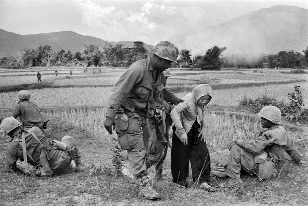 A U.S. air cavalryman lends a helping hand to an aged Vietnamese woman who grew tired as she and her neighbors were being resettled from their village to a refugee camp, Jan. 5, 1968. Other villagers had refused to assist her because, according to custom, they would then have borne responsibility for her for the remainder of her life. (AP Photo/Dang Van Phuoc)