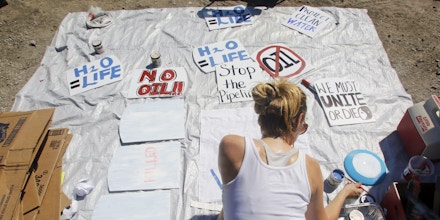 Casey Stinenetz, St. Louis, paints signs against the Dakota Access Pipeline for people to hold during a protest against the Dakota Access Pipeline which took place at a pipeline construction site Saturday Sept. 17, 2016, in Montrose, Iowa. (Erin Lefevre/The Hawk Eye via AP)