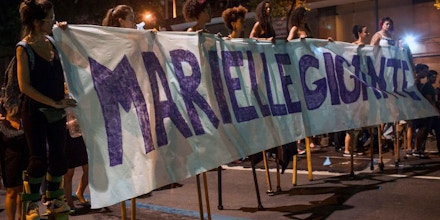 A group of women on stilts hold a banner reading 