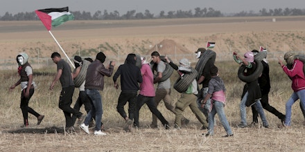 Palestinian masked protesters carrying tires walk toward the border fence during clashes with Israeli troops along Gaza's border with Israel, east of Khan Younis, Gaza Strip, Thursday, April 5, 2018. An Israeli airstrike in northern Gaza early on Thursday killed a Palestinian, while a second man died from wounds sustained in last week's mass protest. The fatalities bring to 21 the number of people killed in confrontations in the volatile area over the past week with a new round of protests along the border is expected on Friday. (AP Photo/Adel Hana)