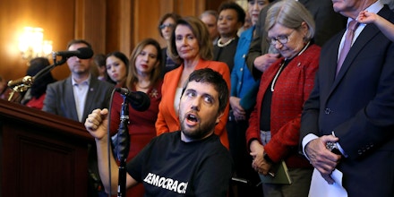 WASHINGTON, DC - DECEMBER 19:  Ady Barkan (C), who lives with Amyotrophic Lateral Sclerosis, delivers remarks during a rally organized by House Minority Leader Nancy Pelosi (D-CA) in the Rayburn Room at the U.S. Capitol December 19, 2017 in Washington, DC. Pelosi and fellow House Democrats invited people with complex medical needs and disabilities who rely on Medicare to rally with them before the House was to vote on the Tax Cuts and Jobs Act. (Photo by Chip Somodevilla/Getty Images)