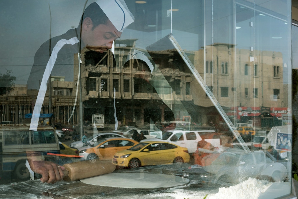 A damaged building is seen in the reflection of a bakery window in Mosul's al-Jadidah district.