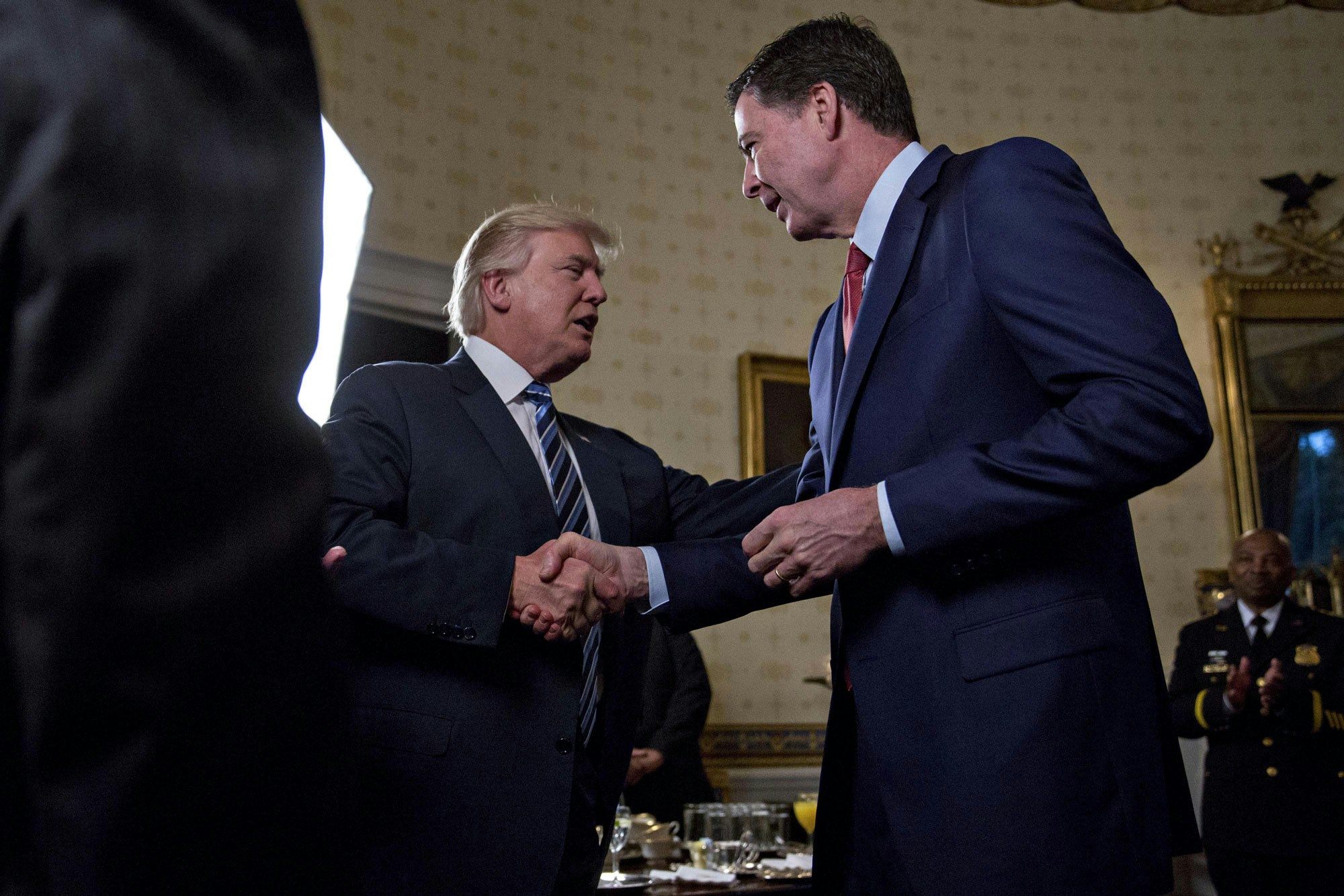 U.S. President Donald Trump, center, shakes hands with James Comey, director of the Federal Bureau of Investigation (FBI), during an Inaugural Law Enforcement Officers and First Responders Reception in the Blue Room of the White House in Washington, D.C., U.S., on Sunday, Jan. 22, 2017. Trump today mocked protesters who gathered for large demonstrations across the U.S. and the world on Saturday to signal discontent with his leadership, but later offered a more conciliatory tone, saying he recognized such marches as a hallmark of our democracy. Photographer: Andrew Harrer/Bloomberg via Getty Images