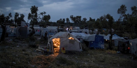 In this Saturday, May 5, 2018 photo a Syrian man reads inside his tent at a makeshift camp outside Moria on the northeastern Aegean island of Lesbos, Greece. Currently, asylum seekers on five Aegean Sea islands _ Lesbos, Chios, Samos, Leros, and Kos _ are banned from traveling onto the Greek mainland as part of the European Union’s controversial “containment policy.” (AP Photo/Petros Giannakouris)