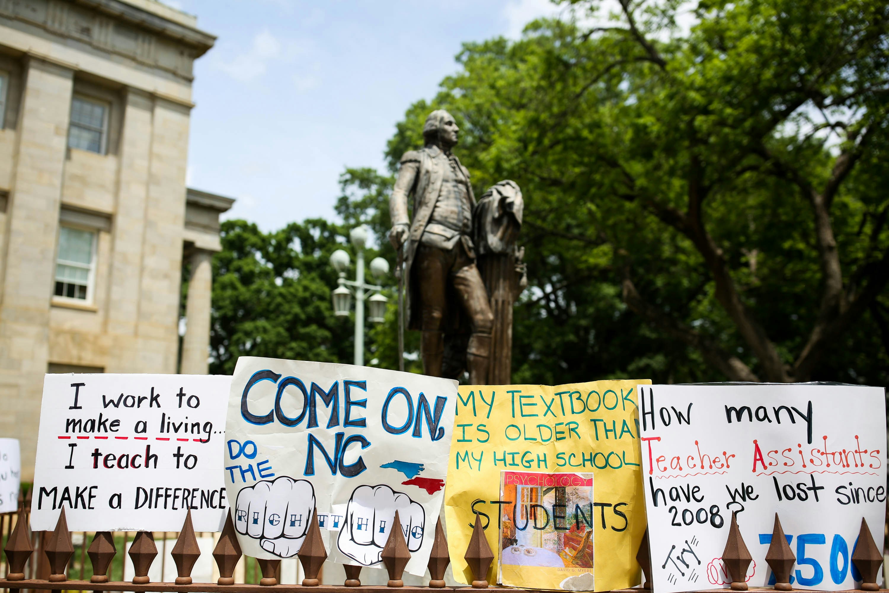 Teachers placed protest signs around a statue of George Washington outside the state capitol building in Raleigh, North Carolina on May, 16 2018. - Tens of thousands of educators, school workers and parents of students marched from the North Carolina Association of Educators building to the State Capitol building to protest wages and per-pupil spending, among other issues. North Carolina ranked 39th in teacher pay last year, according to the National Education Association. Though wages have increased slightly, many educators still believe not enough is being done by state legislature in regards to education funding. (Photo by Logan Cyrus / AFP)        (Photo credit should read LOGAN CYRUS/AFP/Getty Images)