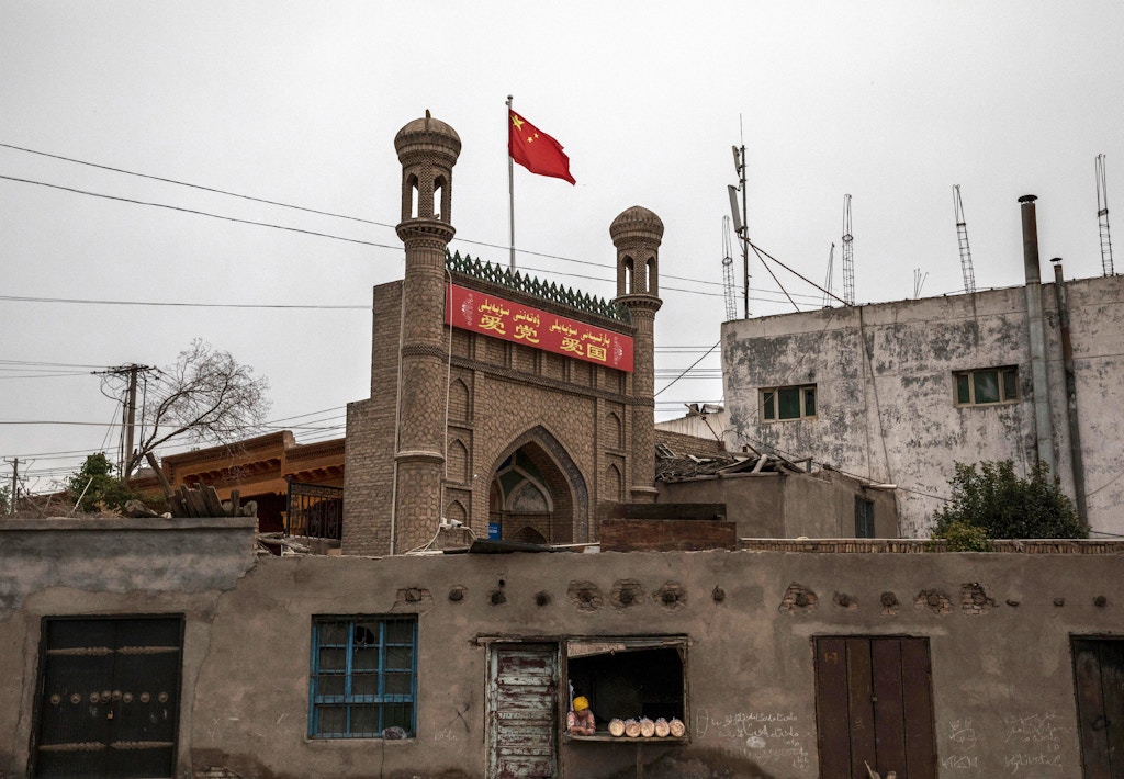 KASHGAR, CHINA - JUNE 28: A Chinese flag flies over a local mosque recently closed by authorities as an ethnic Uyghur woman sells bread at her bakery on June 28, 2017 in the old town of Kashgar, in the far western Xinjiang province, China. Kashgar has long been considered the cultural heart of Xinjiang for the province's nearly 10 million Muslim Uyghurs. At an historic crossroads linking China  to Asia, the Middle East, and Europe, the city has  changed under Chinese rule with government development, unofficial Han Chinese settlement to the western province, and restrictions imposed by the Communist Party. Beijing says it regards Kashgar's development as an improvement to the local economy, but many Uyghurs consider it a threat that is eroding their language, traditions, and cultural identity.  The friction has fuelled a separatist movement that has sometimes turned violent, triggering a crackdown on what China's government considers 'terrorist acts' by religious extremists.  Tension has increased with stepped up security in the city and the enforcement of measures including restrictions at mosques. (Photo by Kevin Frayer/Getty Images)