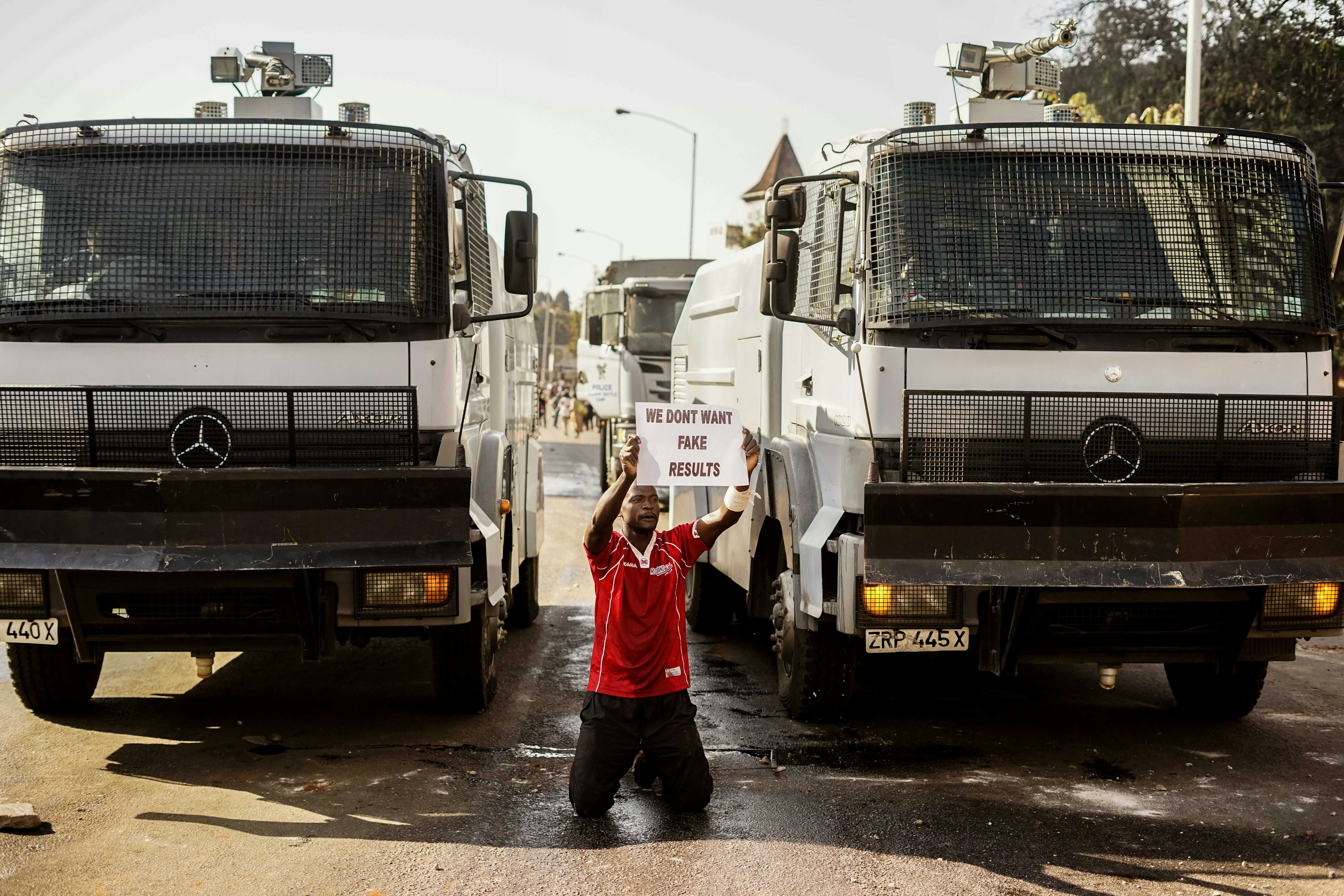 Manifestante segura cartaz enquanto se ajoelha em frente aos canhões de água da polícia em Harare, no dia 1º de agosto de 2018, quando protestos irromperam por conta de suposta fraude nas eleições do Zimbábue.