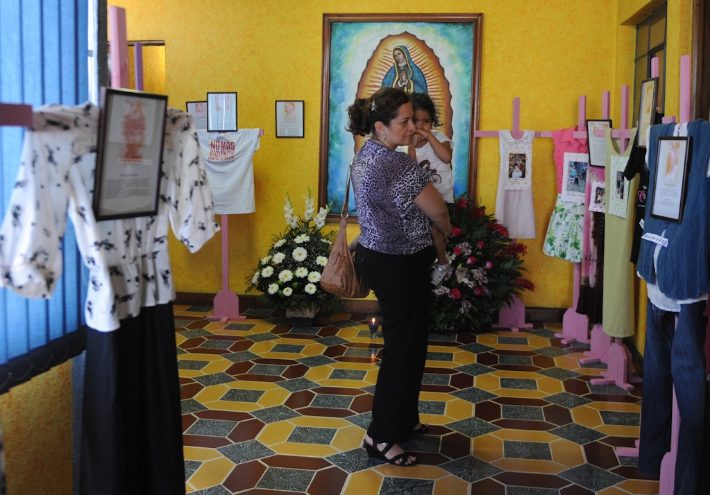 A woman and her daughter look at crosses displaying clothes of women victims of violence during a tribute at the headquarters of the Survivors Foundation in Guatemala City on November 23, 2014, in the framework of the Day for the Elimination of Violence against Women. AFP PHOTO/Johan ORDONEZ (Photo credit should read JOHAN ORDONEZ/AFP/Getty Images)