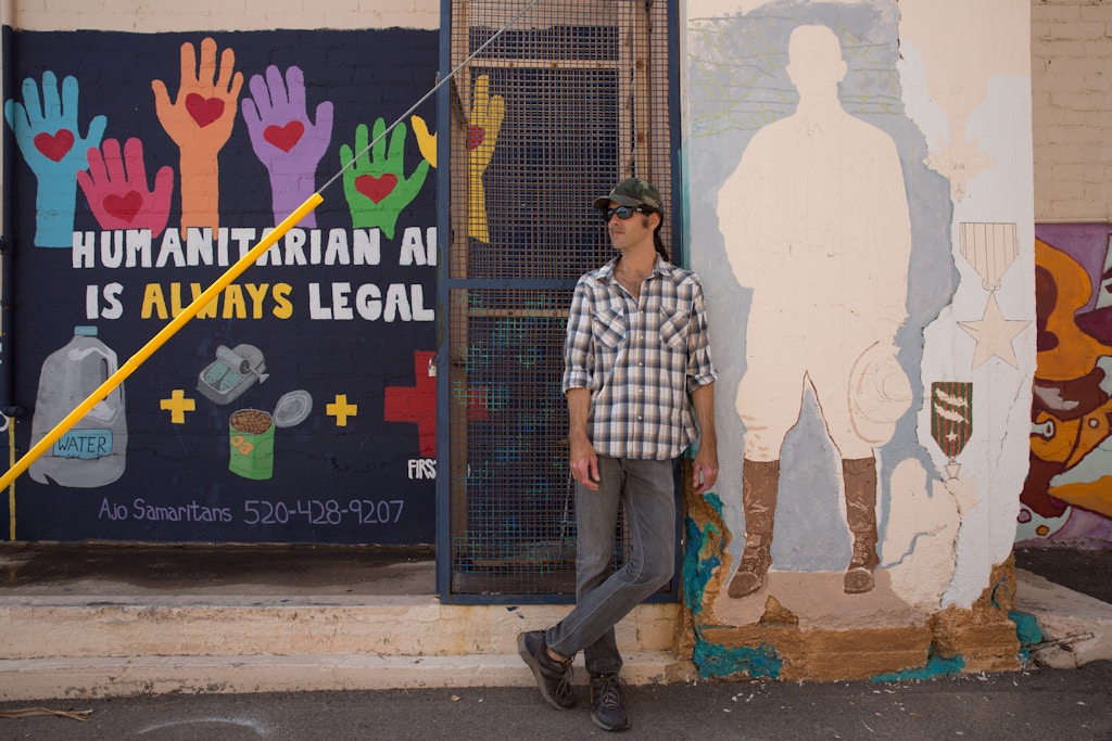 Scott Warren stands next to a community mural project created by the Ajo Samaritans, one of the humanitarian aid groups he works with in the region.