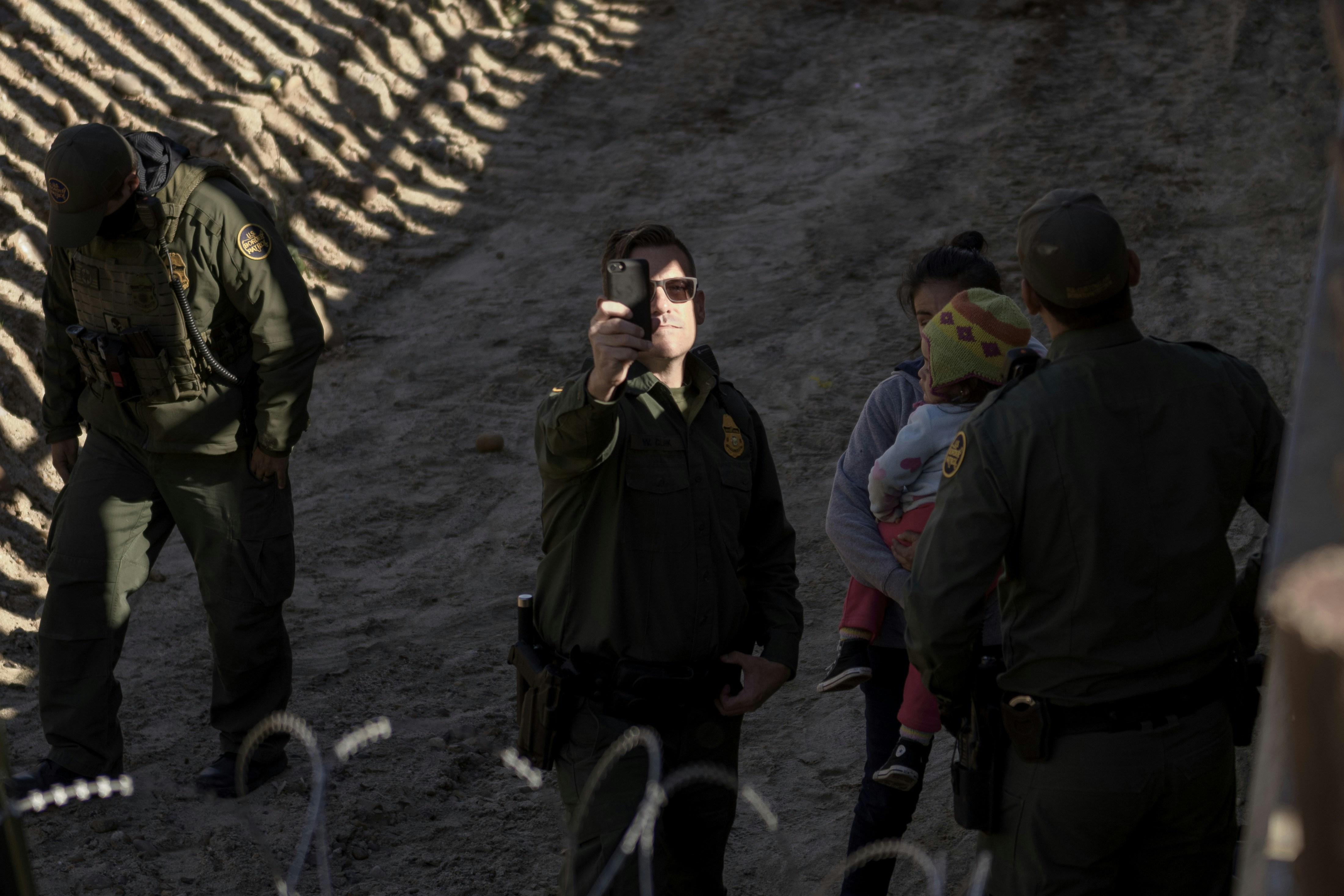 A Border Patrol officers uses his cell phone to take snapshots of the journalists after a Mexican migrant with her daughter jumped the border fence to get into the U.S. side to San Diego, Calif., from Tijuana, Mexico, Saturday, Dec. 29, 2018. Discouraged by the long wait to apply for asylum through official ports of entry, many migrants from recent caravans are choosing to cross the U.S. border wall and hand themselves in to border patrol agents. (AP Photo/Daniel Ochoa de Olza)