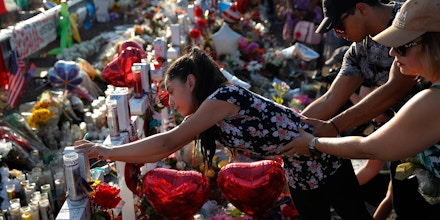 A woman leans over to write a message on a cross at a makeshift memorial at the scene of a mass shooting at a shopping complex, Tuesday, Aug. 6, 2019, in El Paso, Texas. (AP Photo/John Locher)