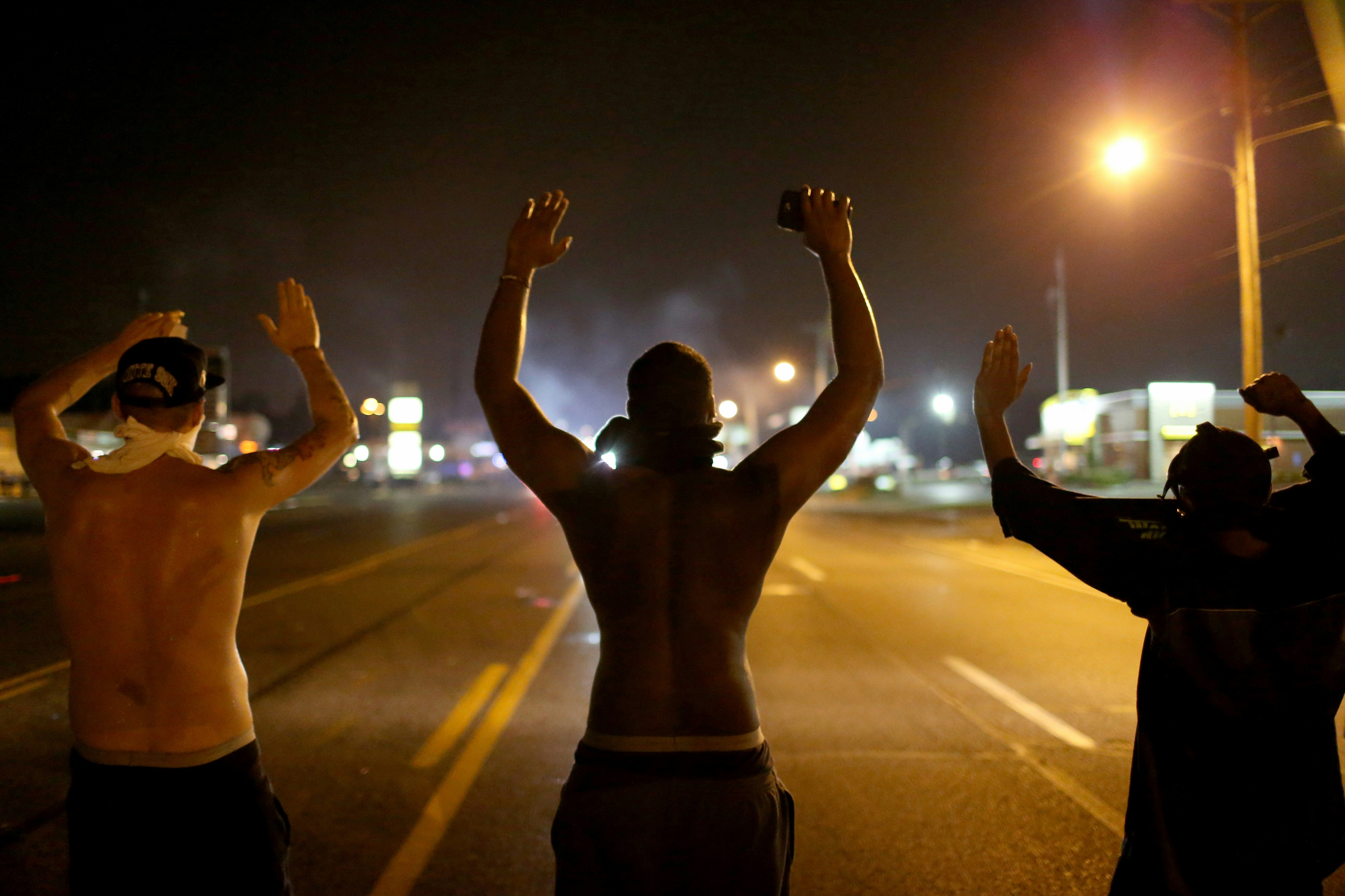 FERGUSON, MO - AUGUST 17:  Demonstrators raise their arms and chant, "Hands up, Don't Shoot", as police clear them from the street as they protest the shooting death of Michael Brown on August 17, 2014 in Ferguson, Missouri. Police sprayed pepper spray, shot smoke, gas and flash grenades as violent outbreaks have taken place in Ferguson since the shooting death of Michael Brown by a Ferguson police officer on August 9th.  (Photo by Joe Raedle/Getty Images)