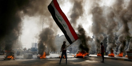 A protester holds an Iraqi flag amid a cloud of smoke from burning tires during ongoing anti-government protests in Najaf, Iraq November 26, 2019. REUTERS/Alaa al-Marjani - RC2ZID9MARY6