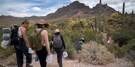 AJO, ARIZONA - MAY 10: Volunteers for the humanitarian aid organization No More Deaths walk with jugs of water for undocumented immigrants on May 10, 2019 near Ajo, Arizona. The volunteers distributed the aid along remote desert trails where immigrants pass after crossing the border from Mexico. The number of immigrant deaths, mostly due to dehydration and exposure, has risen as higher border security in urban border areas has pushed immigrant crossing routes into more remote desert regions. No More Deaths volunteer Scott Warren is scheduled to appear in federal court on May 29 in Tucson, charged by the U.S. government on two counts of harboring and one count of conspiracy for providing food, water, and beds to two Central American immigrants in January, 2018. If found guilty Warren could face up to 20 years in prison. The trial is seen as a watershed case by the Trump Administration, as it pressures humanitarian organizations working to reduce suffering and deaths of immigrants in remote areas along the border. The government claims the aid encourages human smuggling. In a separate misdemeanor case, federal prosecutors have charged Warren with abandonment of property, for distributing food and water along migrant trails.  (Photo by John Moore/Getty Images)