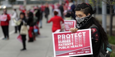 March 23, 2020 - Oakland, California, United States: Valeria Vital, an ER tech, stands holding a sign during a protest by medical professionals working for Kaiser Permanente in Oakland and their supporters. The medical care professionals hoped to emphasize their need for better personal protective equipment (PPE) rather than having to use bandanas instead as they say Kaiser has asked them to do. (Carlos Avila Gonzalez / San Francisco Chronicle / Polaris) ///