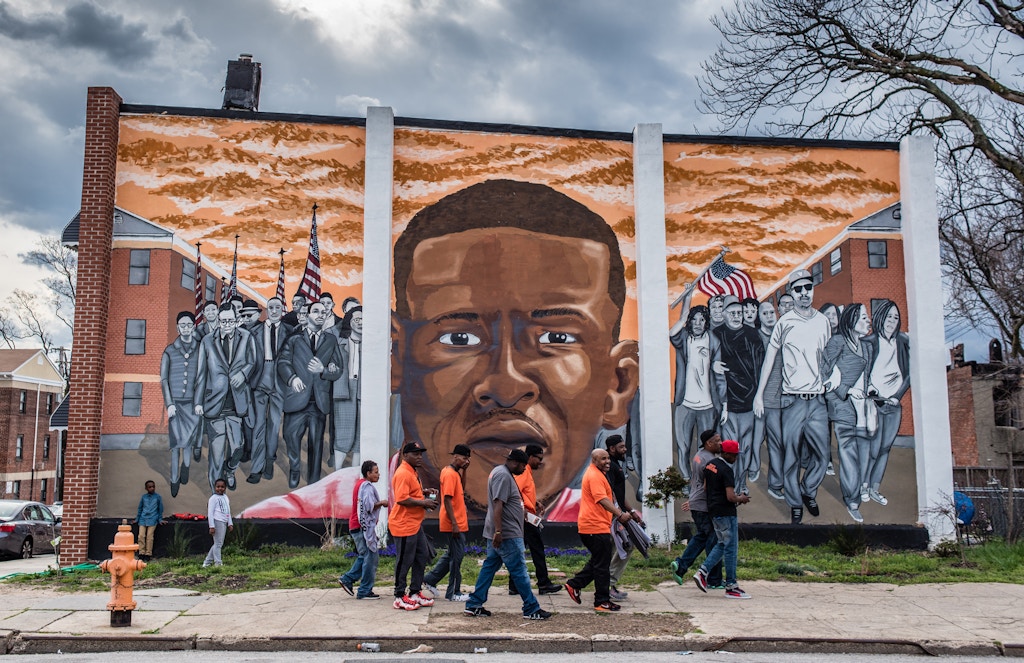 Safe Streets workers walk past a mural of Freddie Gray, painted by the artist Nether, in Sandtown-Winchester in West Baltimore in 2016.