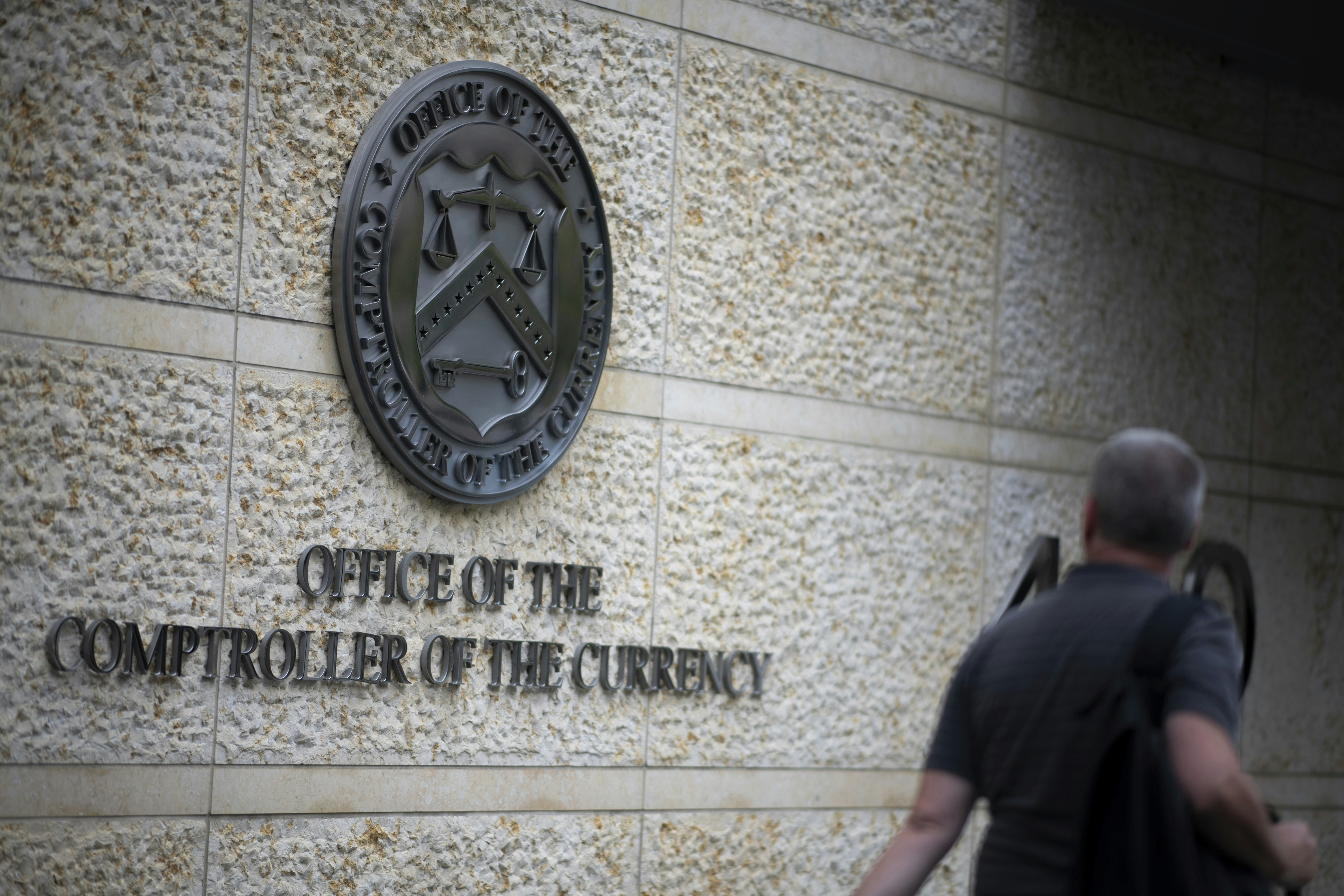 A man walks by the Office of the Comptroller of the Currency logo as it appears on OCC headquarters in Washington, D.C., as seen on September 9, 2019.
