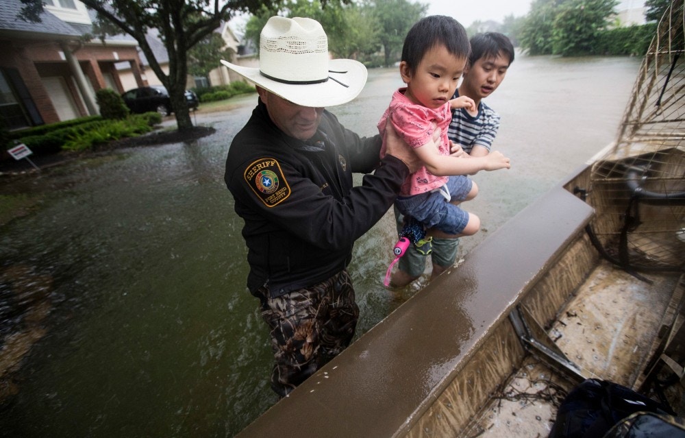 Fort Bend County Sheriff Troy Nehls and Lucas Wu lift Ethan Wu into an airboat as they are evacuated from rising waters from Tropical Storm Harvey, at the Orchard Lakes subdivision on Sunday, Aug. 27, 2017, in unincorporated Fort Bend County, Texas. (Brett Coomer/Houston Chronicle via AP)