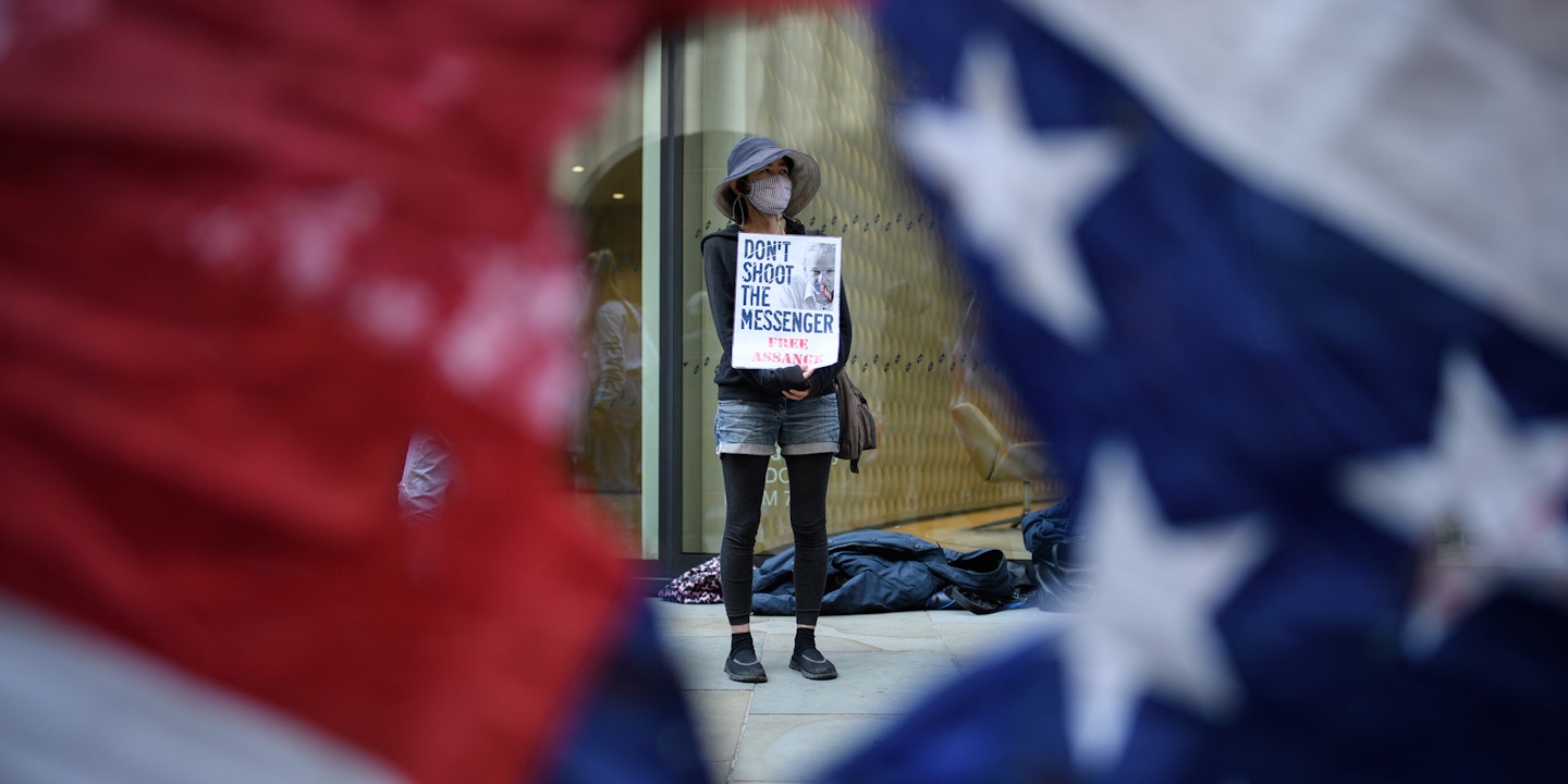 Supporters of the Wikileaks founder Julian Assange are seen through a torn U.S. flag as they gather outside the Old Bailey in London on Sept. 14, 2020. 