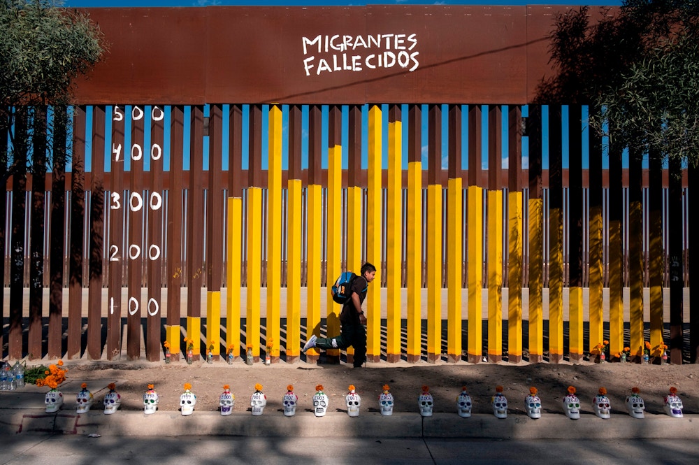 Junior Hernandez, a migrant from Guatemala, runs next to the border fence where he and members of the Coalicion Pro Defensa del Migrante (Pro Defense of the Migrant Coalition) painted a graph showing statistics of dead migrants, on the Mexican side of the US-Mexico border in Tijuana, Baja California state, Mexico, on November 2, 2019. - According to the coalition the goal of the painting is to 'give visibility' to the amount of dead migrants on their journey to the United States and the impact of new migration policies both on the US and Mexico. (Photo by Guillermo Arias / AFP) (Photo by GUILLERMO ARIAS/AFP via Getty Images)