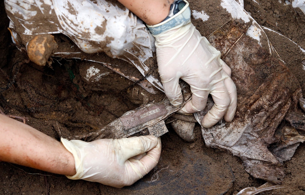 FALFURRIAS, TX - JUNE 10: A member of the Baylor forensics team holds a piece of clothing found beside the body of an unidentified migrant who apparently died crossing the border and ended up buried anonymously in a pauper's grave for another team member to document in Falfurrias, TX on June 10, 2014. (Photo by Jessica Rinaldi/The Boston Globe via Getty Images)