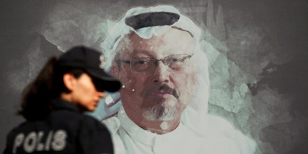 FILE - In this Wednesday, Oct. 2, 2019 file photo, a Turkish police officer walks past a picture of slain Saudi journalist Jamal Khashoggi prior to a ceremony, near the Saudi Arabia consulate in Istanbul, marking the one-year anniversary of his death. A Turkish court is scheduled Friday, July, 3, 2020, to begin the trial in absentia of two former aides of Saudi Crown Prince Mohammed bin Salman and 18 other Saudi nationals over the 2018 killing. Turkish prosecutors have indicted the 20 Saudi nationals over Khashoggi's grisly killing at the Saudi Consulate in Istanbul that cast a cloud of suspicion over Prince Mohammed. (AP Photo/Lefteris Pitarakis, File)