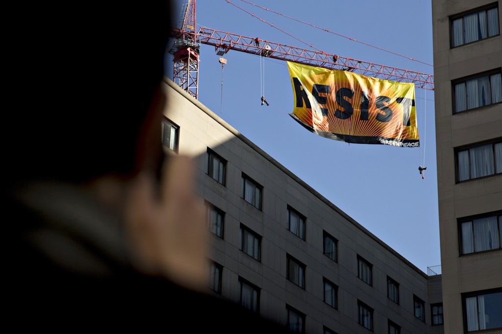 An onlooker takes photographs of Greenpeace activists hanging from a construction crane with a banner that reads "Resist" in Washington, D.C., U.S., on Wednesday, Jan. 25, 2017. The protest comes one day after the Trump administration invited TransCanada Corp. to reapply for its Keystone XL project and issued a memorandum supporting completion of the Energy Transfer Partners LPs Dakota Access Pipeline. Photographer: Andrew Harrer/Bloomberg via Getty Images