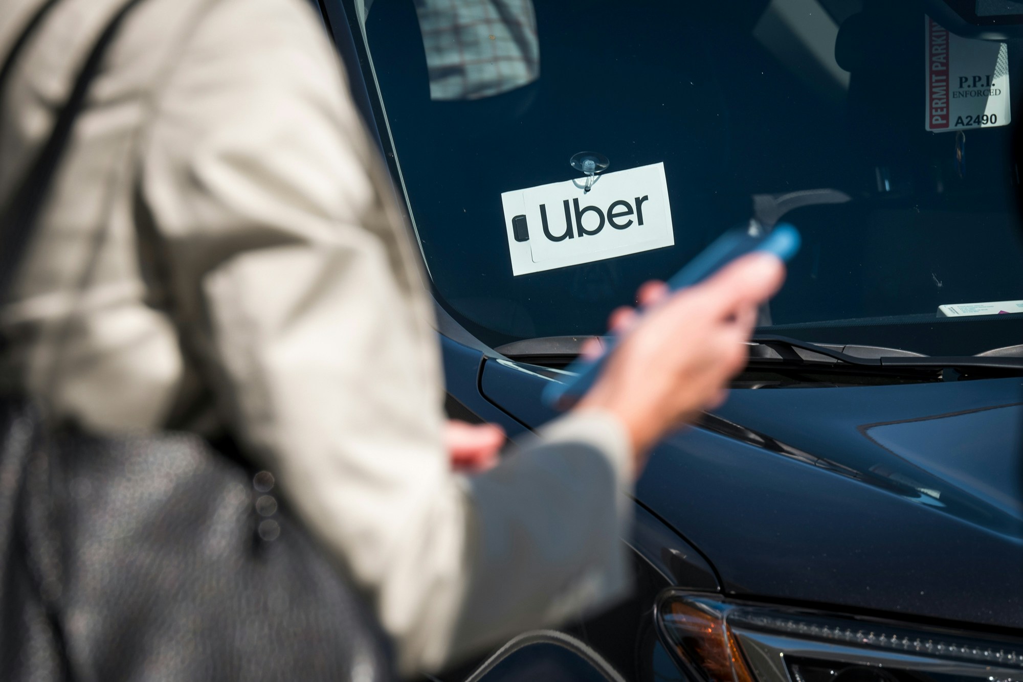 A traveler uses a smartphone in front of a vehicle displaying Uber Technologies Inc. signage at the Oakland International Airport in Oakland, California, U.S., on Tuesday, Aug. 6, 2019. Uber Technologies Inc. is scheduled to release earnings figures on August 8. Photographer: David Paul Morris/Bloomberg via Getty Images