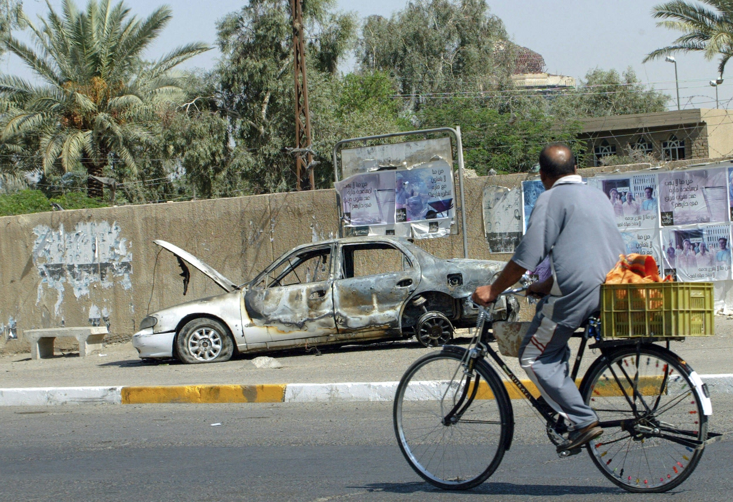 An Iraqi man rides a bicycle passing by a remains of a car in Baghdad, 20 September 2007. The car was burnt during the incident  when Blackwater guards escorting US embassy officials opened fire in a Baghdad neighbourhood, 16 September 2007, killing 10 people and wounding 13.  Iraq and the United States agreed to establish a joint commission to examine security of US-government civilians in Iraq following a deadly shooting involving private security firm Blackwater, State Department spokesman Tom Casey said.     AFP PHOTO/ ALI YUSSEF (Photo credit should read ALI YUSSEF/AFP via Getty Images)