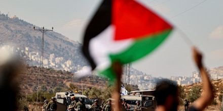 A Palestinian protester facing Israeli security forces, waves a national flag during a demonstration against the establishment of Israeli outposts on their lands, in Beit Dajan, east of Nablus in the Israeli-occupied West Bank, on October 22, 2021. (Photo by ABBAS MOMANI / AFP) (Photo by ABBAS MOMANI/AFP via Getty Images)