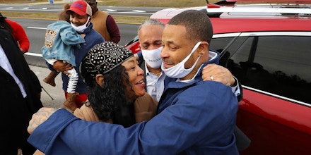 Devonia Inman, front right, is embraced by his mother, Dinah Ray, and stepfather, David Ray, after being released from custody at Augusta State Medical Prison, background, having served 23 years in prison for a wrongful conviction on Monday, Dec. 20, 2021, in Grovetown, Ga. His charges were dismissed in a murder case. At left is his son Travenski Jackson and granddaughter Alona. (Curtis Compton/Atlanta Journal-Constitution via AP)